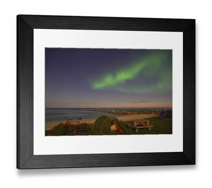 Framed Print : Green northern lights and stars in the sky above a beach with tent and bicycle at night