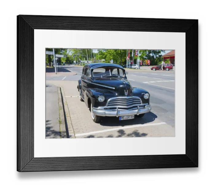 Framed Print : A black vintage car is parked in a car park on a road