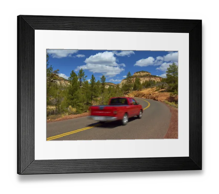 Framed Print : A red pickup truck drives on a winding road through a scenic mountain region with trees and blue sky