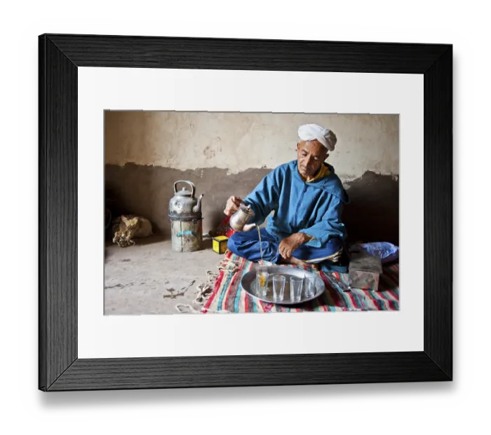 Framed Print : Elderly Berber man wearing a turban sitting on the floor on a rug pouring traditional mint tea from a silver jug