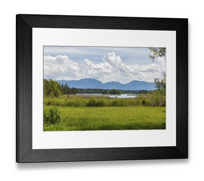Framed Print : A lake with grassy meadows and mountains in the background under a cloudy sky