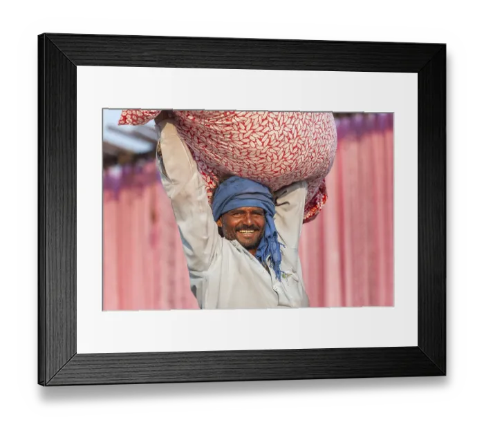Framed Print : Man carrying a bundle of cloth on his head in front of pink fabric panels