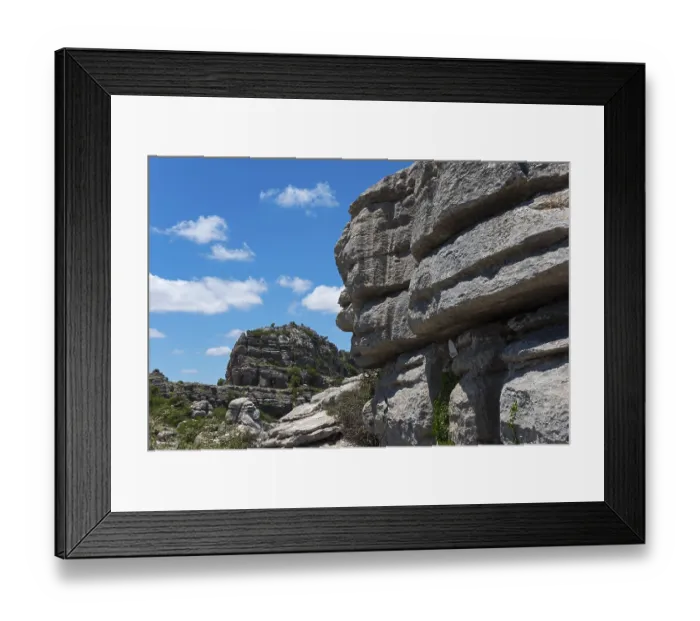 Framed Print : Close-up of large rocks with blue sky and clouds in the background and green vegetation