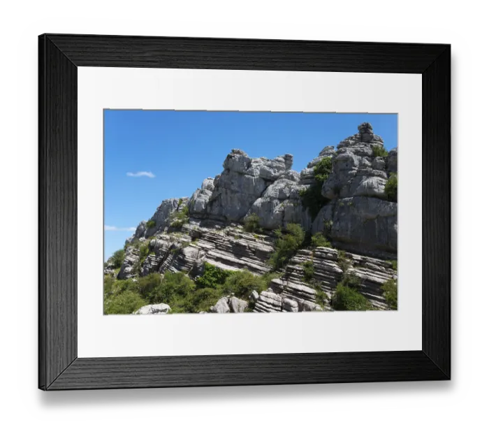 Framed Print : Rock layers and vegetation on a steep rock face under a bright blue sky