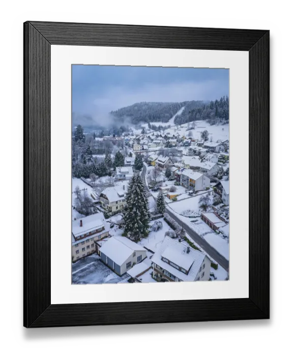 Framed Print : Aerial view of a snow-covered village surrounded by forests and mountains in winter Framed Print : Aerial view of a snow-covered village surrounded by forests and mountains in winter