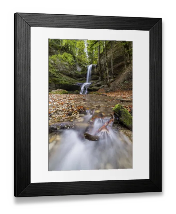 Framed Print : A quiet stream flows over small waterfalls through a forest with stones and tree trunks