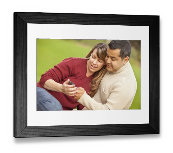 Framed Print : Attractive mixed-race couple enjoying their camera phone in the park