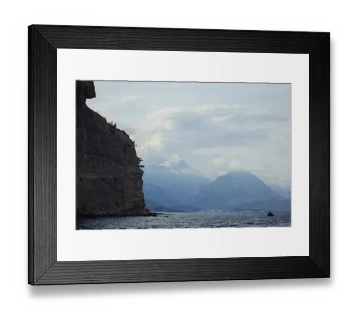 Framed Print : Scenic view of a rocky shoreline with distant mountains under a cloudy sky