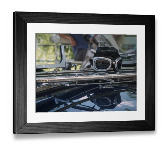 Framed Print : Close-up of a driver's goggles with reflection on the windscreen of a classic car against a blurred road