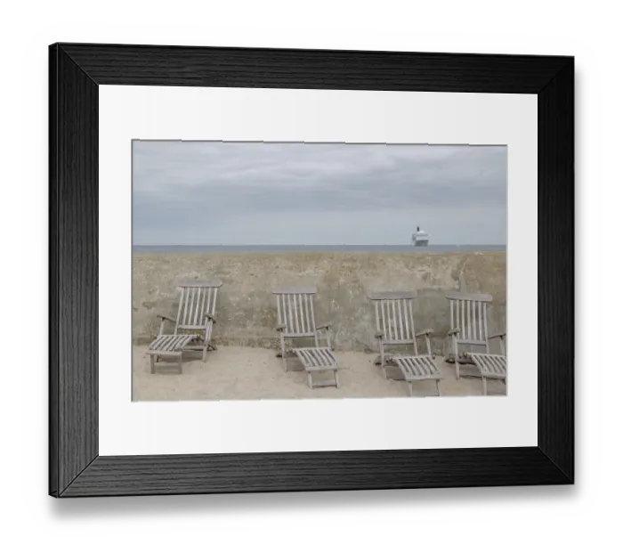 Framed Print : Abandoned deckchairs on the beach in front of a concrete wall with a cruise ship in the background
