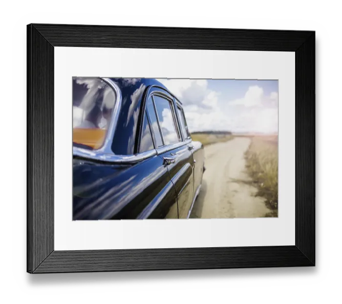 Framed Print : A blue vintage car on a rural road under a cloudy sky