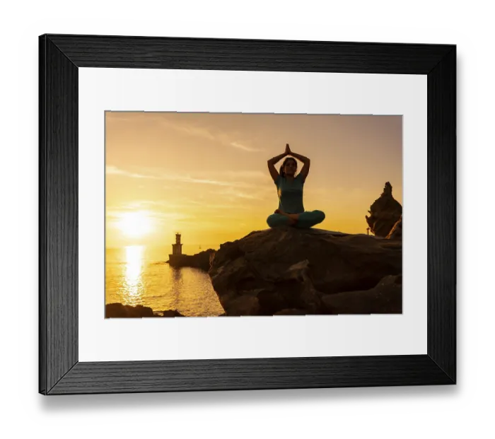 Framed Print : A woman doing meditation and yoga exercises at sunset next to a lighthouse in the sea