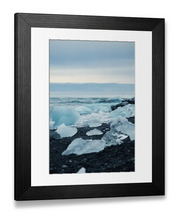 Framed Print : Blue ice pieces on black sand by a calm ocean