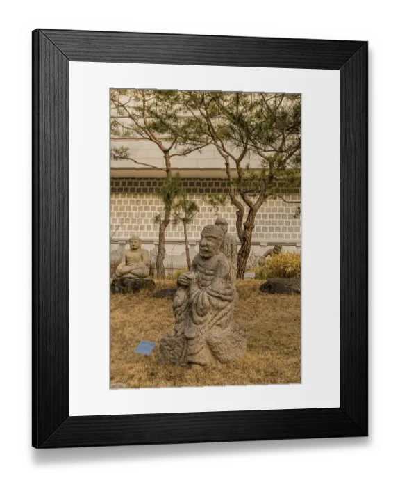 Framed Print : Stone carved statue of Buddhist deity vajraputra in front of white wall in garden in South Korea