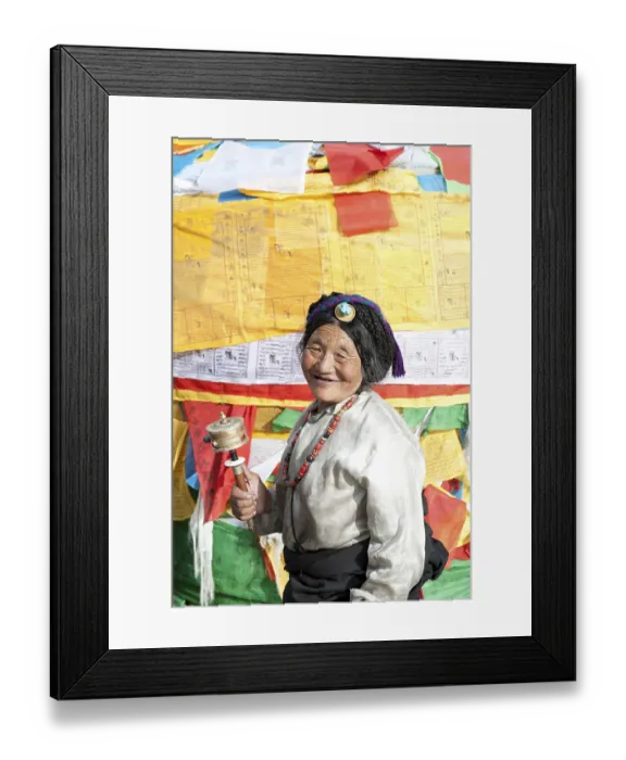 Framed Print : Tibetan Buddhism, devout Tibetan with prayer wheel in front of colorful prayer flags