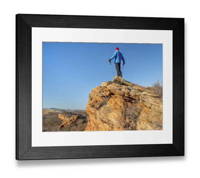 Framed Print : Male hiker with trekking poles on a sandstone cliff against blue sky