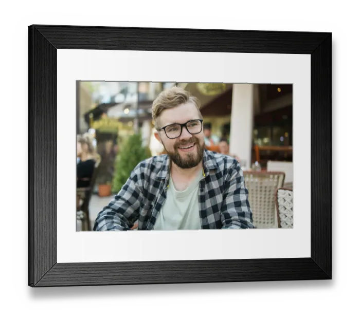 Framed Print : Bearded man in glasses laughing joyfully while sitting at a cafe table outdoors