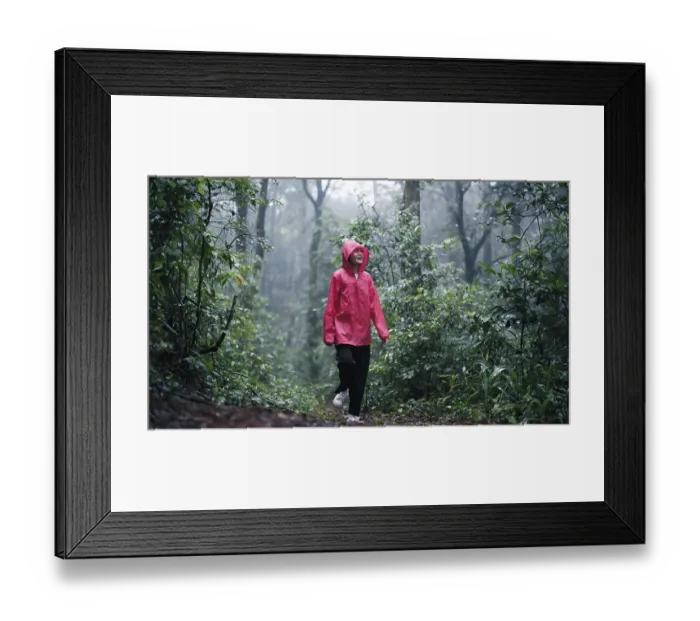 Framed Print : A smiling woman in a red raincoat hiking through a lush