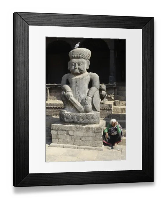 Framed Print : Old woman seated by a large stone statue of a Malla wrestler in front of Dattatreya Temple