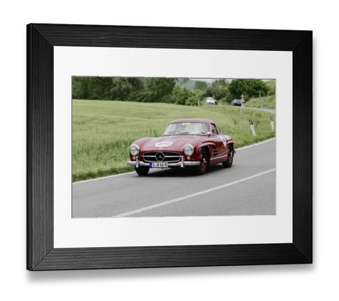 Framed Print : Red Mercedes on country road from the front in green landscape