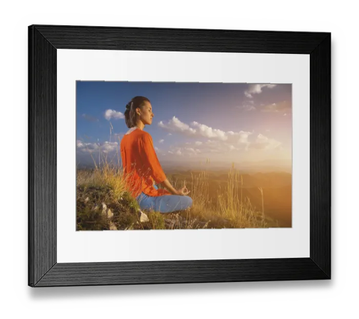 Framed Print : Young caucasian woman meditates in the lotus position in the grass in the mountains near the cliff in the setting sun
