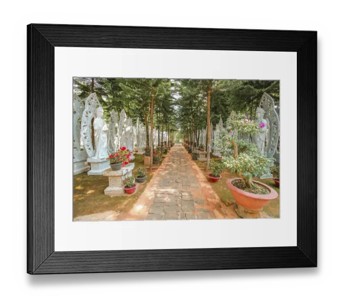 Framed Print : Serene walkway surrounded by trees and Buddhist sculptures illuminated by sunlight