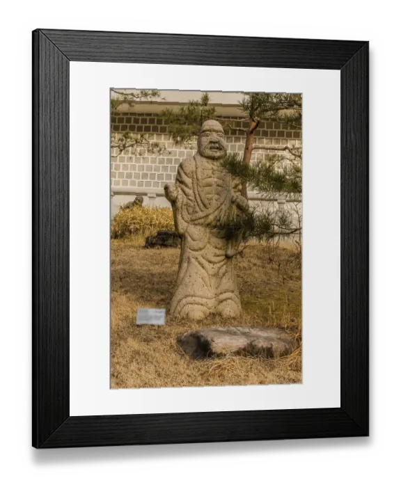 Framed Print : Stone carved statue of Buddhist deity kanakavatsa in front of white wall in garden in South Korea