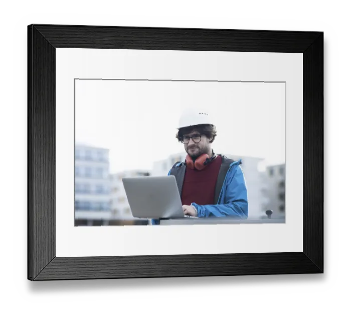 Framed Print : Young engineer with helmet and hearing protection checks outside work with laptop Framed Print : Young engineer with helmet and hearing protection checks outside work with laptop