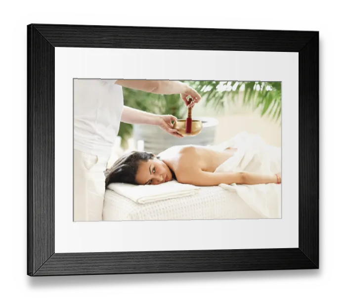 Framed Print : Side view of female therapist using singing bowl over back of relaxed Asian woman in spa salon