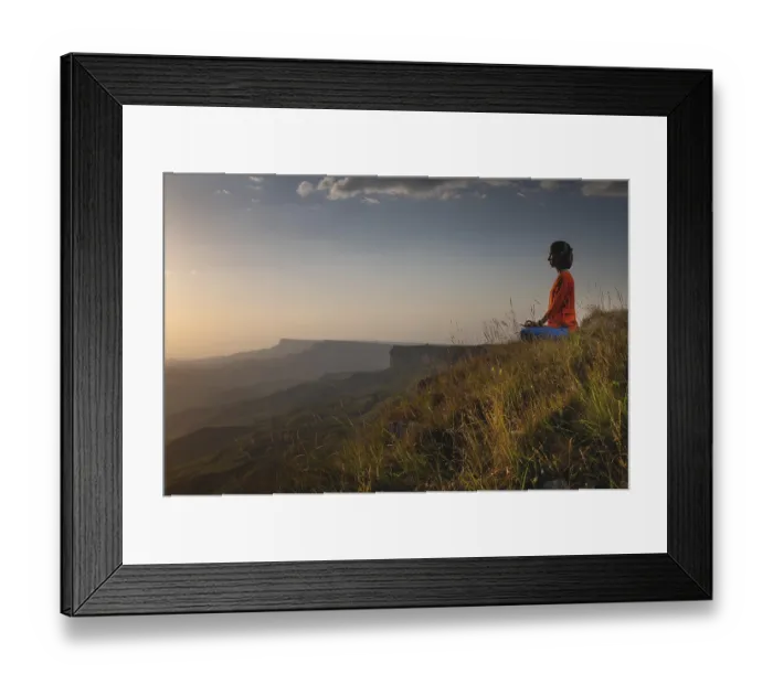 Framed Print : Meditating woman sitting in lotus position near a cliff at sunset overlooking the mountains
