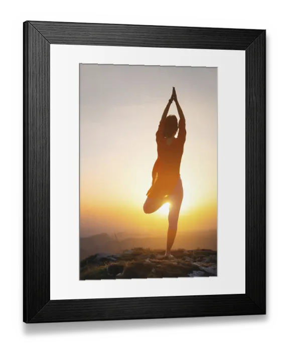 Framed Print : A woman stands in a yoga pose against the sun in the mountains