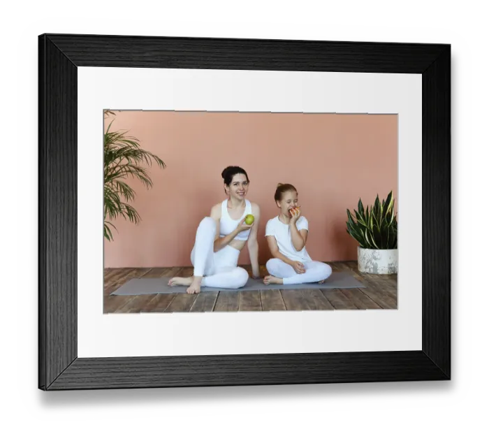 Framed Print : Smiling woman and little girl eating fruits after practicing yoga on mat in cozy living room