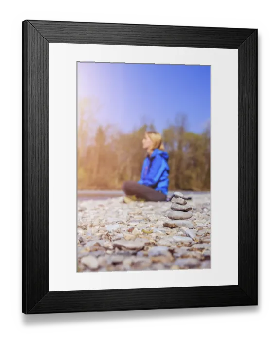 Framed Print : Cairn on a pebble beach, meditating woman in the background Framed Print : Cairn on a pebble beach, meditating woman in the background