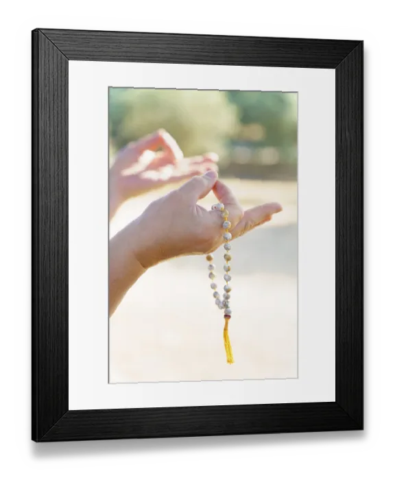 Framed Print : Close-up of a woman's hands holding a sunlit Buddhist mala praying in a field at sunset Close-up of a woman's