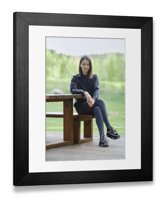 Framed Print : A young woman sits on a wooden bench beside a table