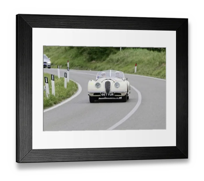 Framed Print : Retro white sports car driving on a winding country road through a green landscape under a blue sky