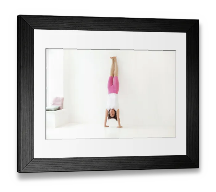 Framed Print : Full body of focused slim female female performing handstand near wall while practicing yoga in light room by