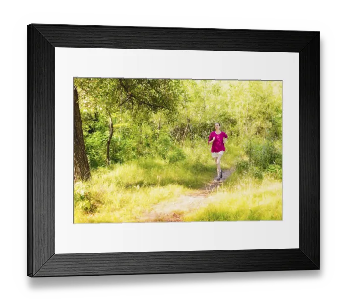 Framed Print : A happy senior woman is running toward the light in the forest during a warm summer day