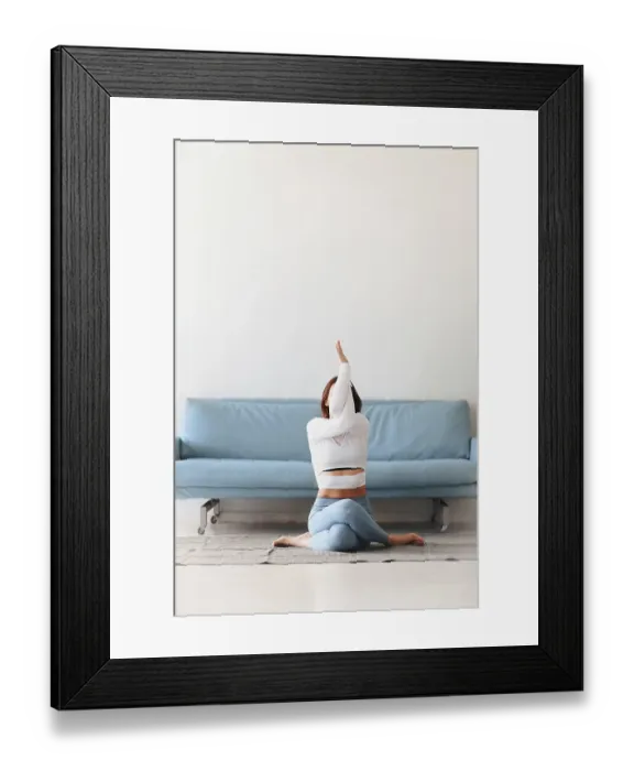 Framed Print : Slim female in sportswear bending aside while practicing yoga near sofa at home