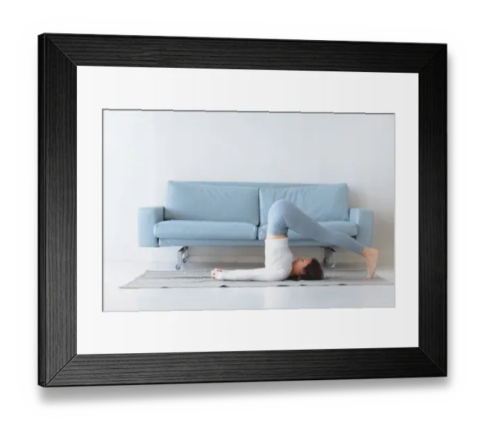 Framed Print : Slim female in sportswear bending aside while practicing yoga near sofa at home