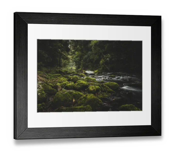 Framed Print : A river flows through a forest with moss-covered rocks and green trees