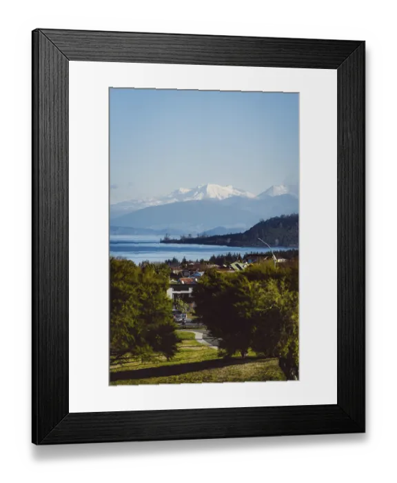 Framed Print : View of snow-capped mountains and a lake with a village in the foreground under a clear sky