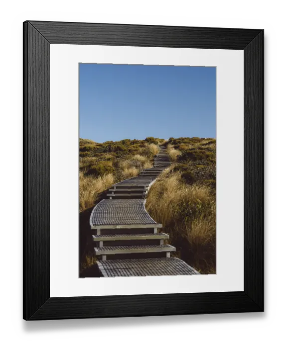 Framed Print : A winding wooden walkway leads through a grassy landscape towards the hill