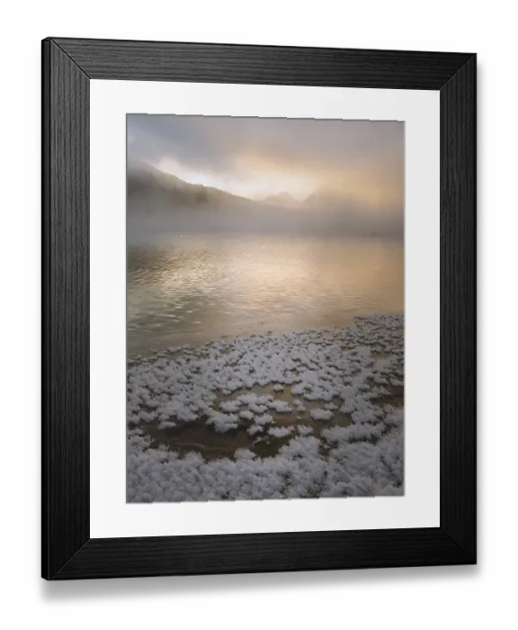 Framed Print : Snow-covered lake shore with distant misty mountains under a golden sunrise
