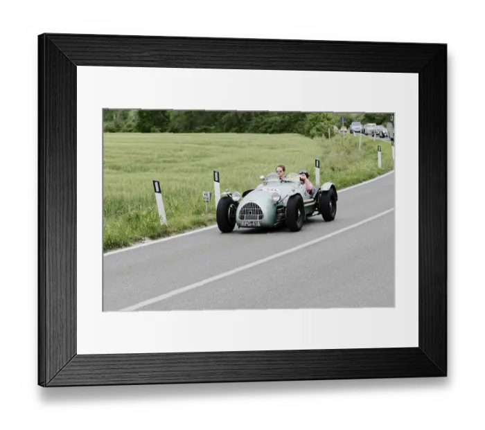 Framed Print : A grey vintage racing car drives on a rural road through green nature