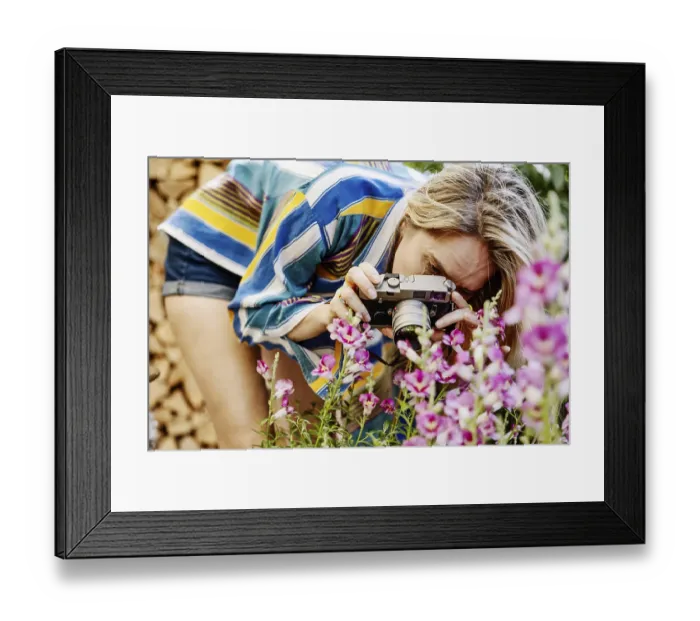 Framed Print : Germany, young woman photographing blooming flowers in the garden