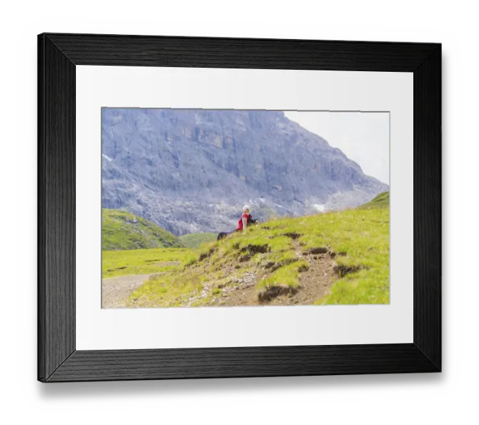 Framed Print : Person sitting on a green meadow with rocky mountains in the background
