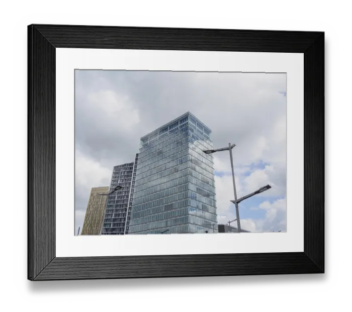 Framed Print : A modern building with a glass facade rises into the cloudy sky Framed Print : A modern building with a glass facade rises into the cloudy sky