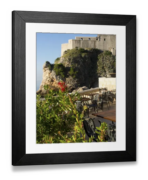 Framed Print : Terrace with chairs and tables next to a rock formation with sea view and historic fortress Framed Print : Terrace with chairs and tables next to a rock formation with sea view and historic fortress