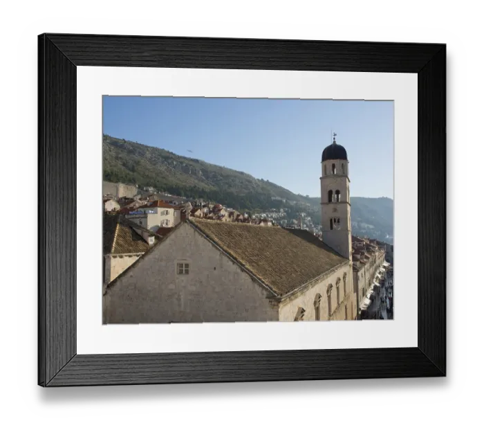 Framed Print : A bell tower rises above a church in a medieval town that stretches along a sunlit hill